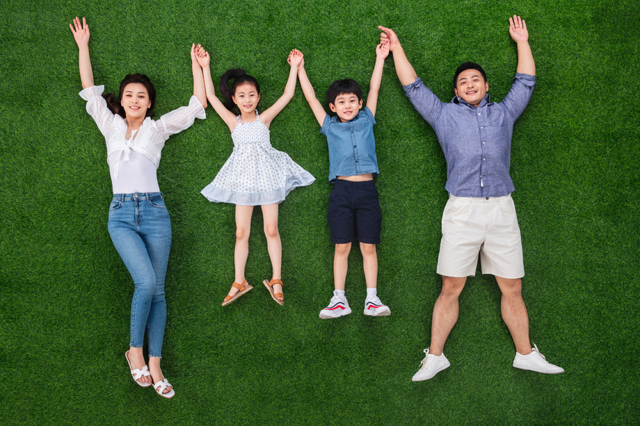 幸福的一家四口手牵手躺在草地上