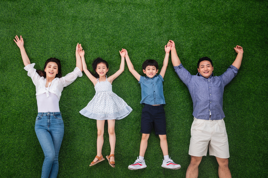 幸福的一家四口手牵手躺在草地上