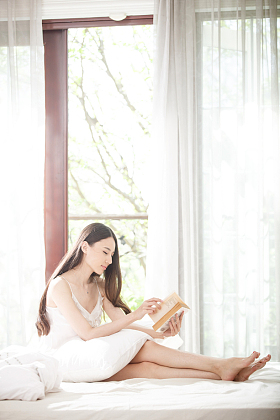 青年女人坐在床上看书照片