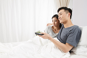 青年情侣坐着床上看电视