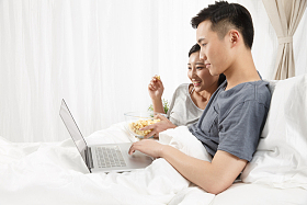 青年情侣坐着床上看电脑