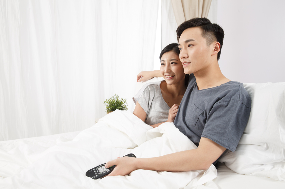 青年情侣坐着床上看电视