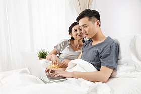 青年情侣坐着床上看电脑