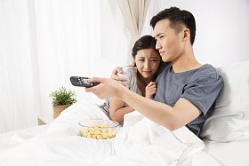 青年情侣坐着床上看电视