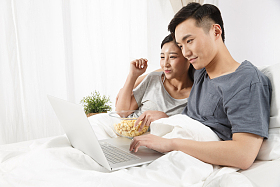 青年情侣坐着床上看电脑