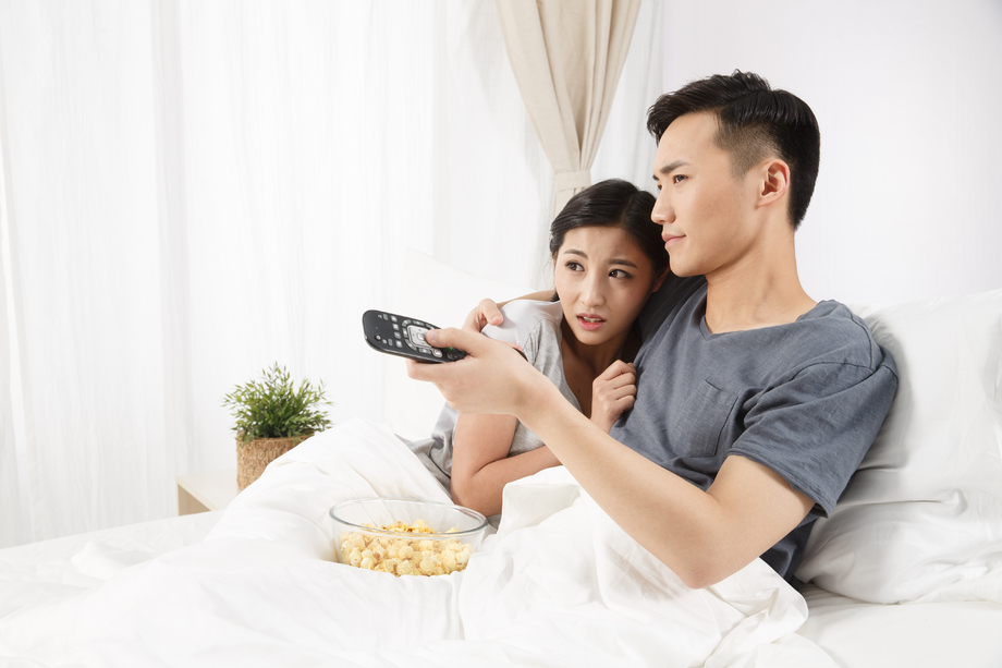 青年情侣坐着床上看电视