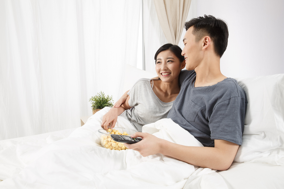青年情侣坐着床上看电视