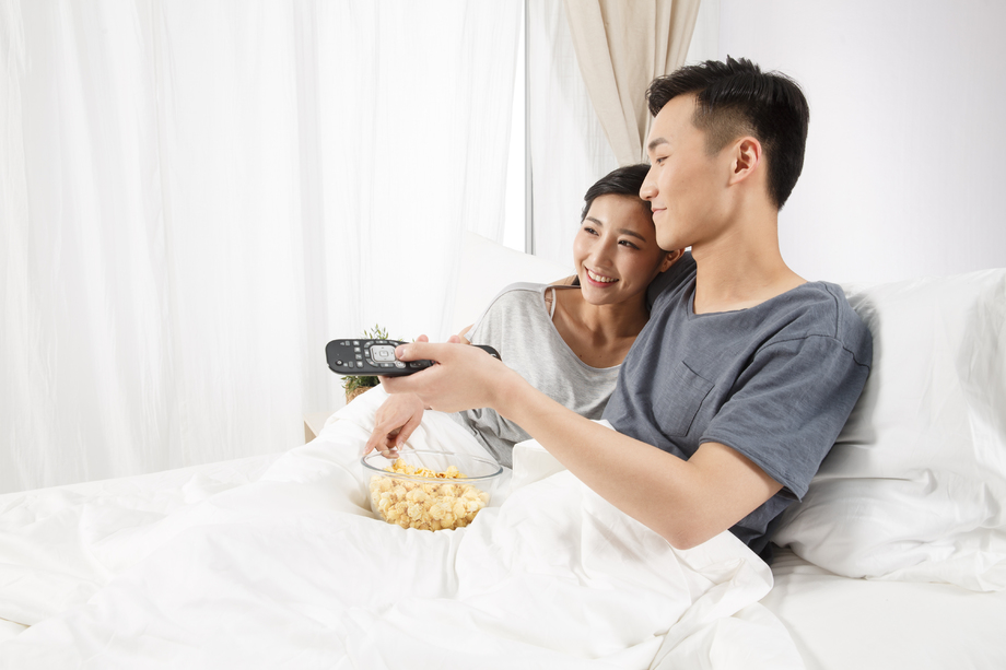 青年情侣坐着床上看电视
