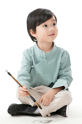 小男孩盘腿坐着拿毛笔写字