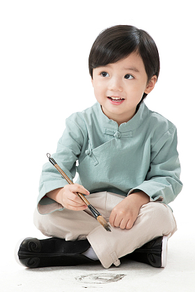 小男孩盘腿坐着拿毛笔写字图片
