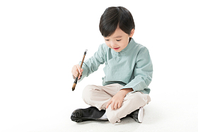 可爱的小男孩坐在地上用毛笔写字