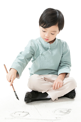 可爱的小男孩坐在地上用毛笔写字