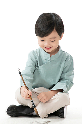 可爱的小男孩坐在地上用毛笔写字