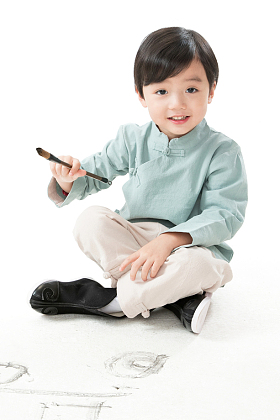 可爱的小男孩坐在地上用毛笔写字