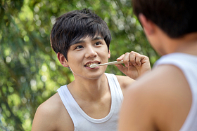 户外对着镜子刷牙的年轻男人