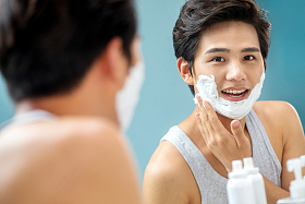 青年男人对着镜子抹剃须膏