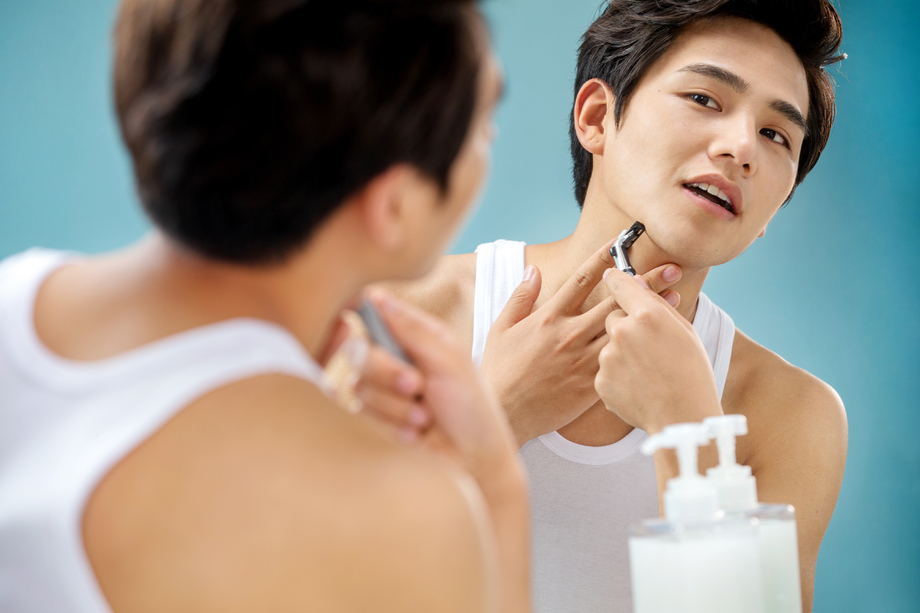 青年男人对着镜子刮胡子 青年男人对着镜子刮胡子