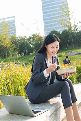 商务女性坐着户外边吃饭边工作