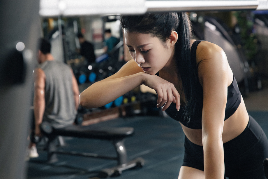 年轻女子趴在健身器材上擦汗 年轻女子趴在健身器材上擦汗