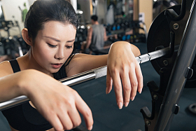 健身房里年轻女子趴在杠铃上休息