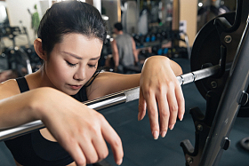 健身房里年轻女子趴在杠铃上休息