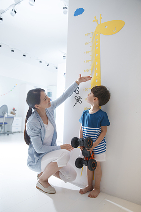 青年女人在为小男孩测量身高照片