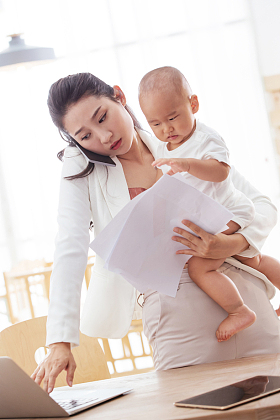 年轻妈妈抱着孩子在家办公图片