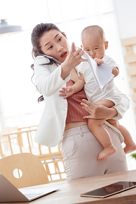 年轻妈妈抱着孩子在家办公照片