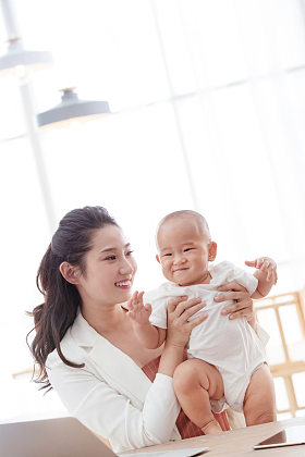 年轻妈妈抱着孩子在家办公图片