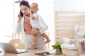 年轻妈妈抱着孩子在家办公图片