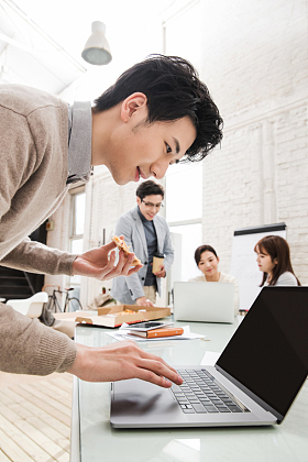 青年商务男士边吃披萨边工作