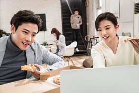 青年商务人士边吃披萨边工作照片