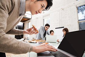 青年商务男士边吃披萨边工作照片