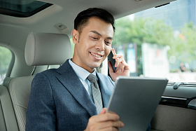 商务男士坐在汽车里拿着平板电脑打电话